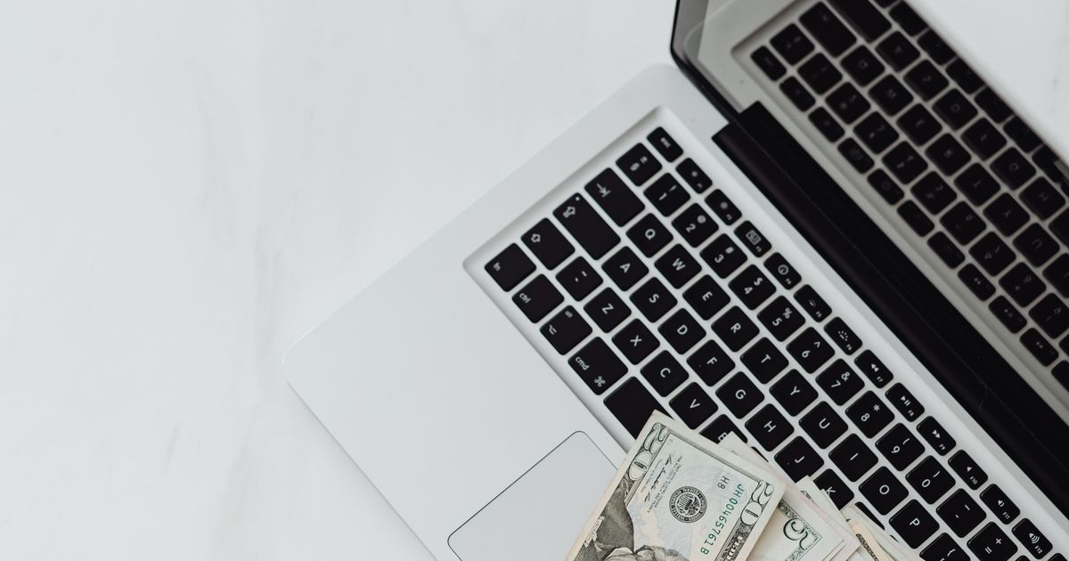 Overhead shot of dollar bills spread across a laptop keyboard — monthly survey earnings